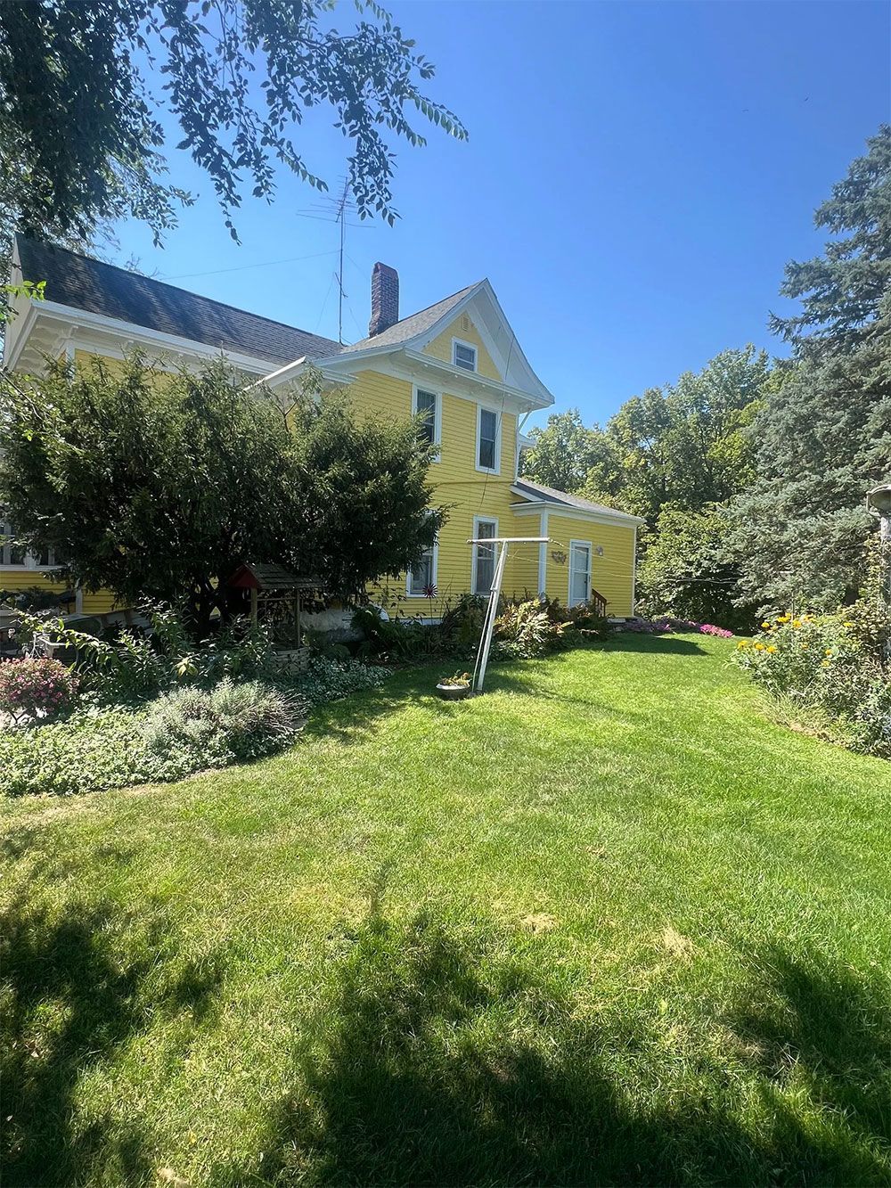 Yellow house with white trim, surrounded by green grass and trees, on a sunny day.