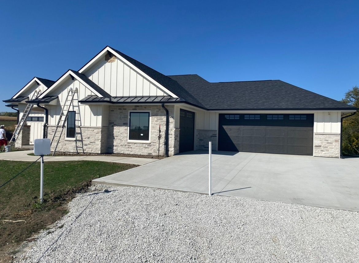 New single-story suburban house with a dark roof, white board-and-batten siding, stone facade, and a two-car garage.