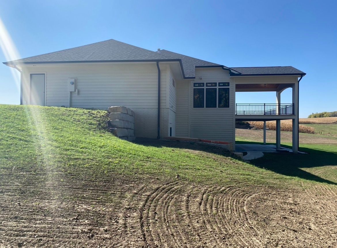 A beige house with a covered deck overlooking an open field under a clear blue sky.