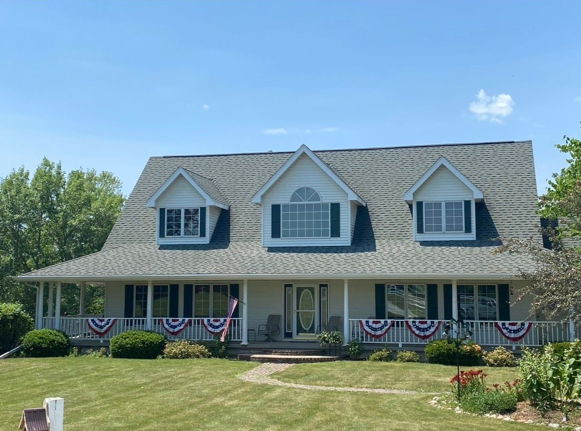 A two-story house with white siding and three dormer windows, featuring a front porch decorated with patriotic bunting.