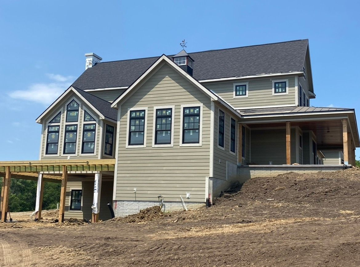 A two-story tan house under construction with black-trimmed windows, a dark roof, and an unfinished wooden deck.