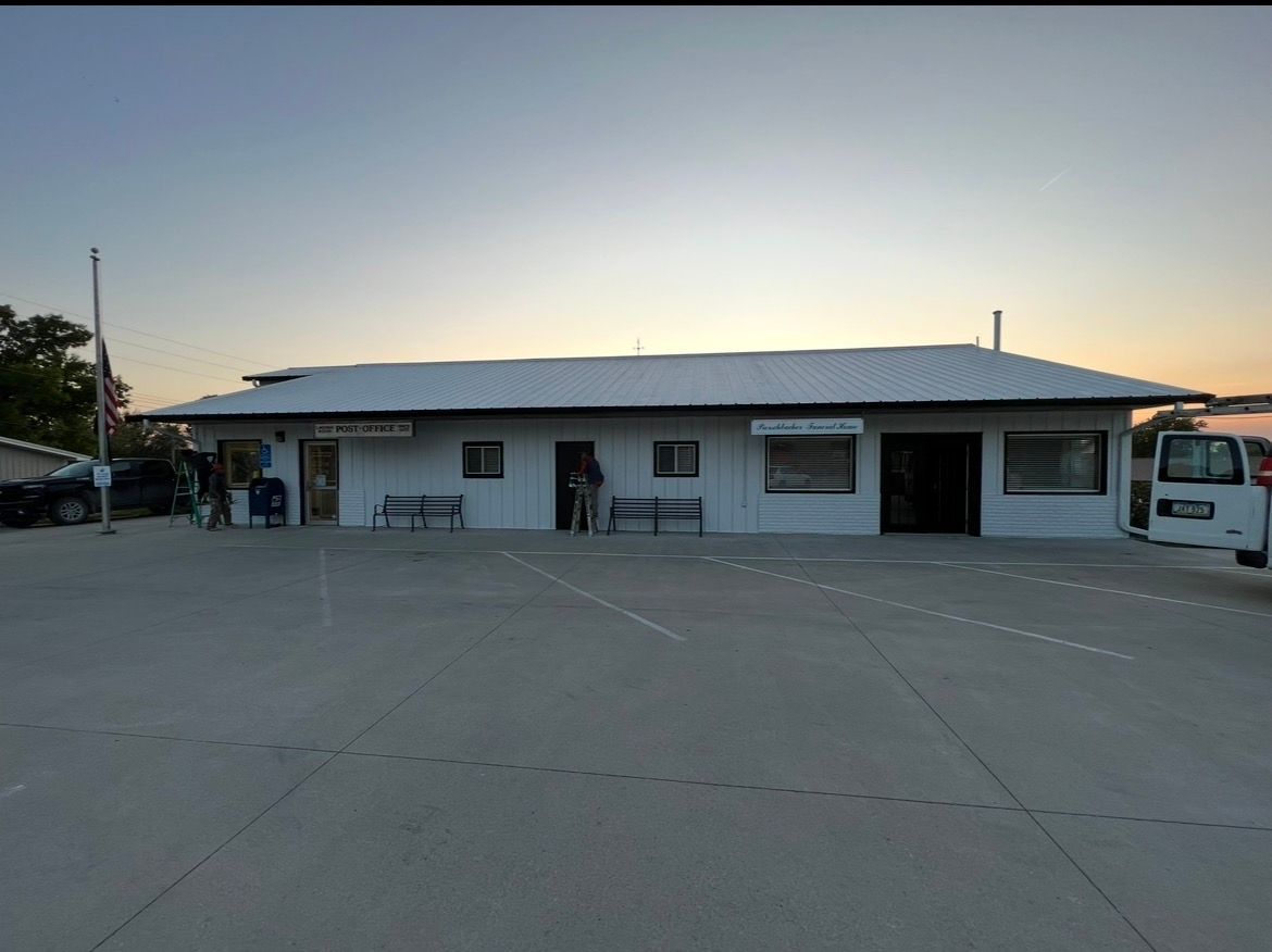 A one-story white building with a metal roof and a parking lot in front during a clear sunset.