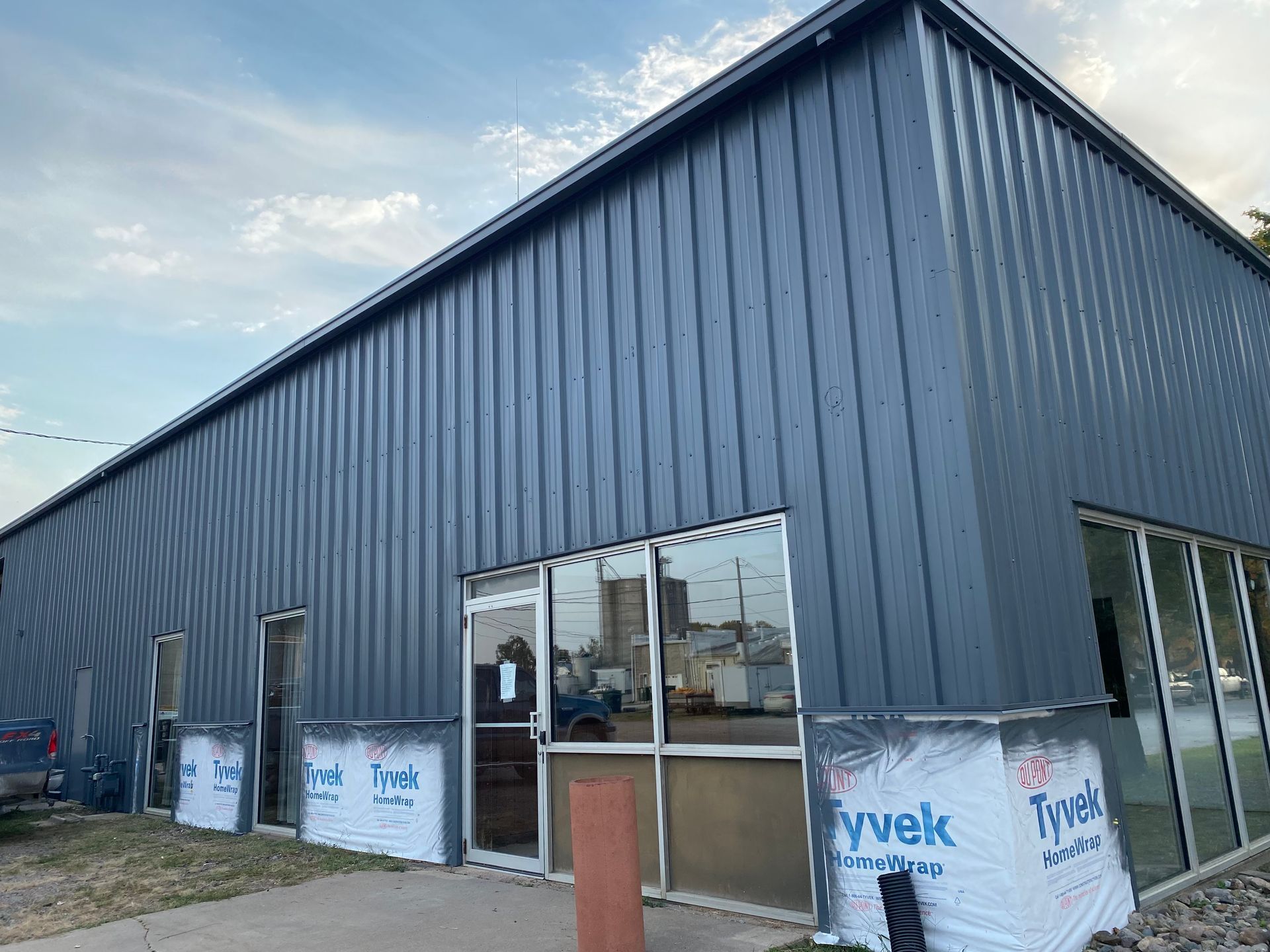 Blue metal-sided building with large windows and a door, Tyvek wrap at the base of the windows.