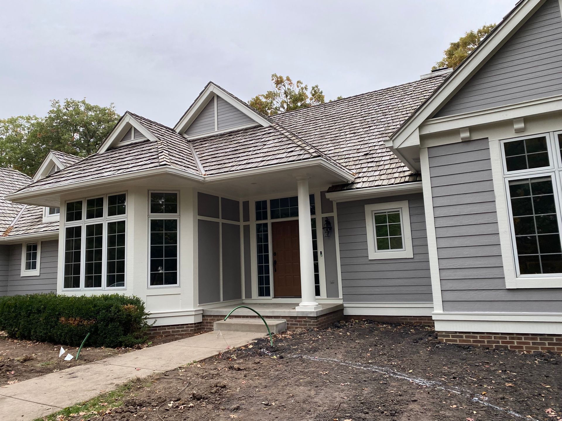 Gray house with patterned roof, white trim, and multiple windows.