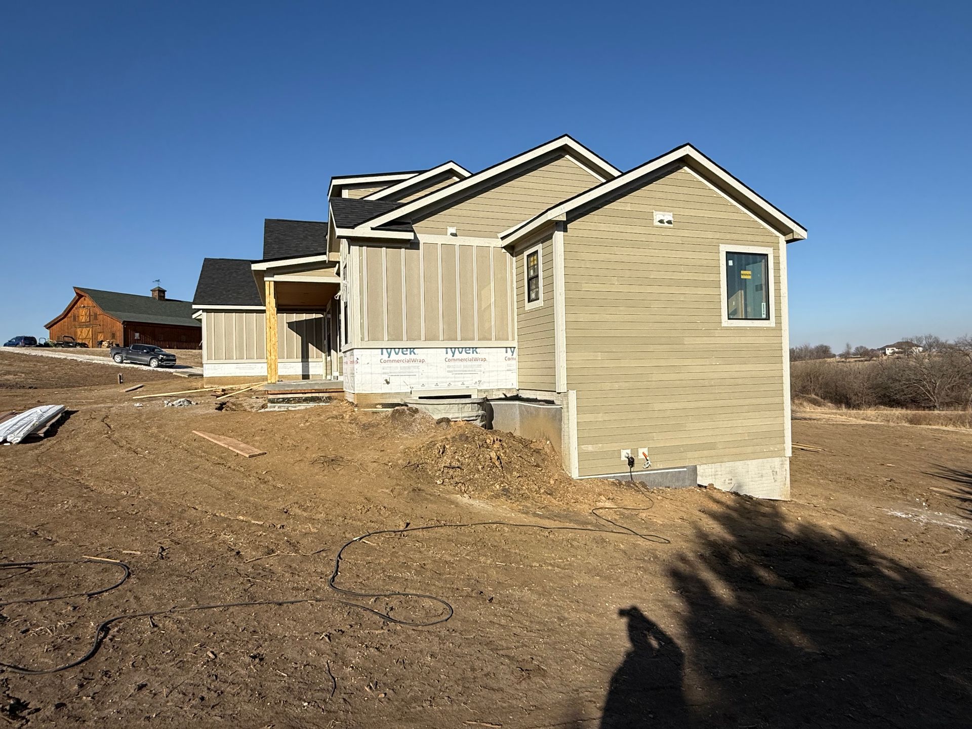 House under construction with tan siding and a dark roof on a sunny day.