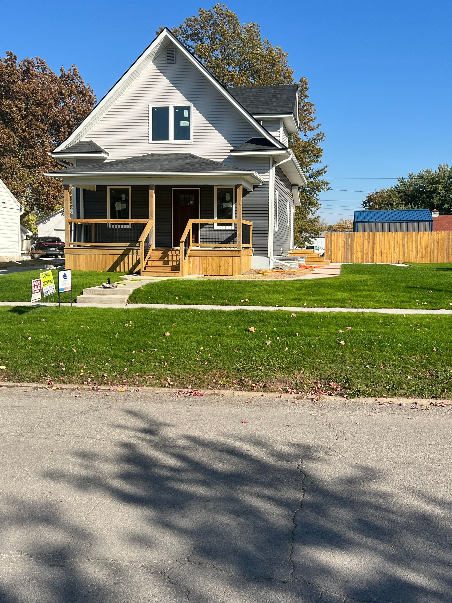 Newly constructed two-story house with gray siding, a wooden porch, and a grassy lawn on a sunny day.