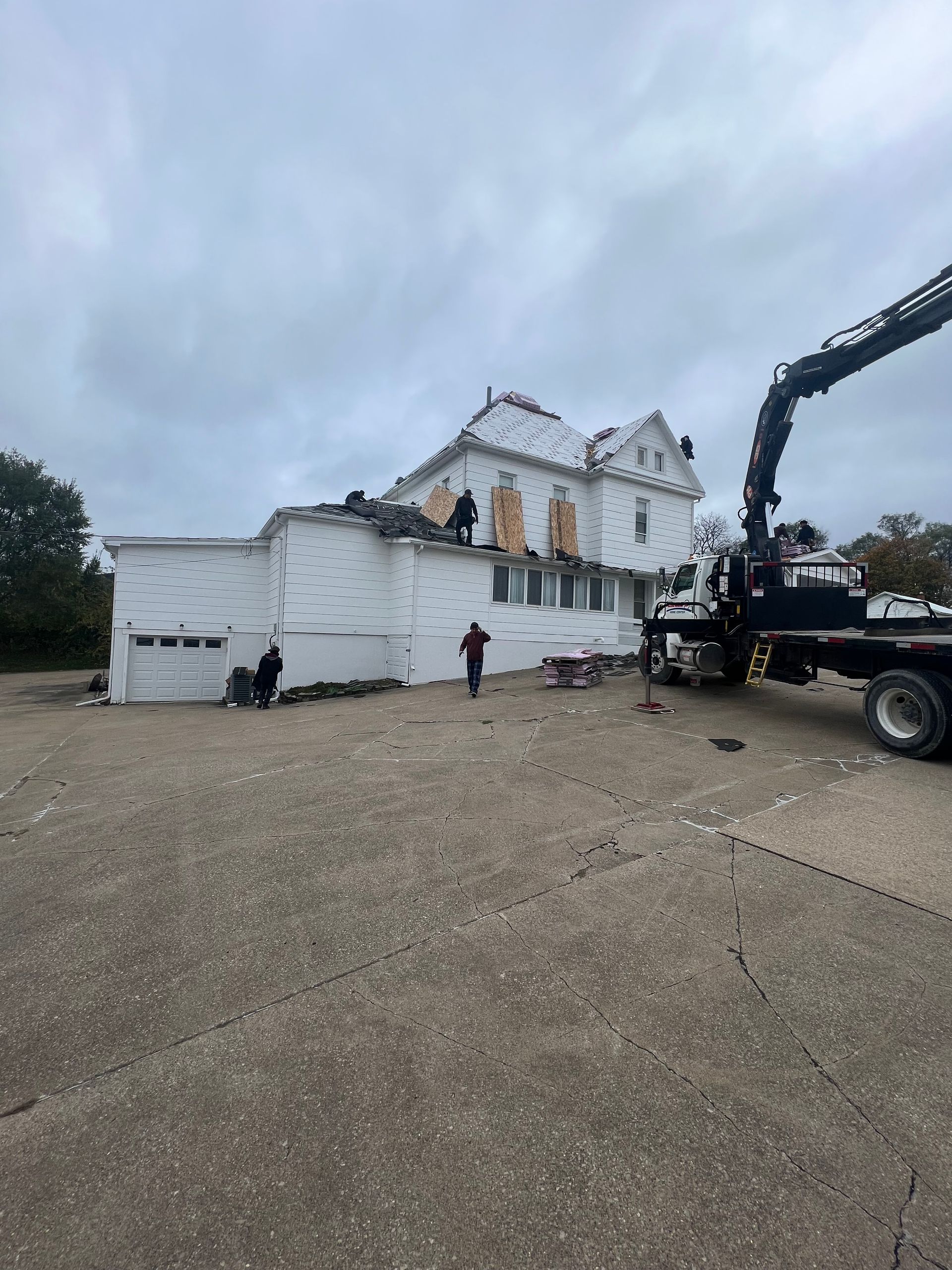 Workers on a white building roof with a crane; cloudy sky.