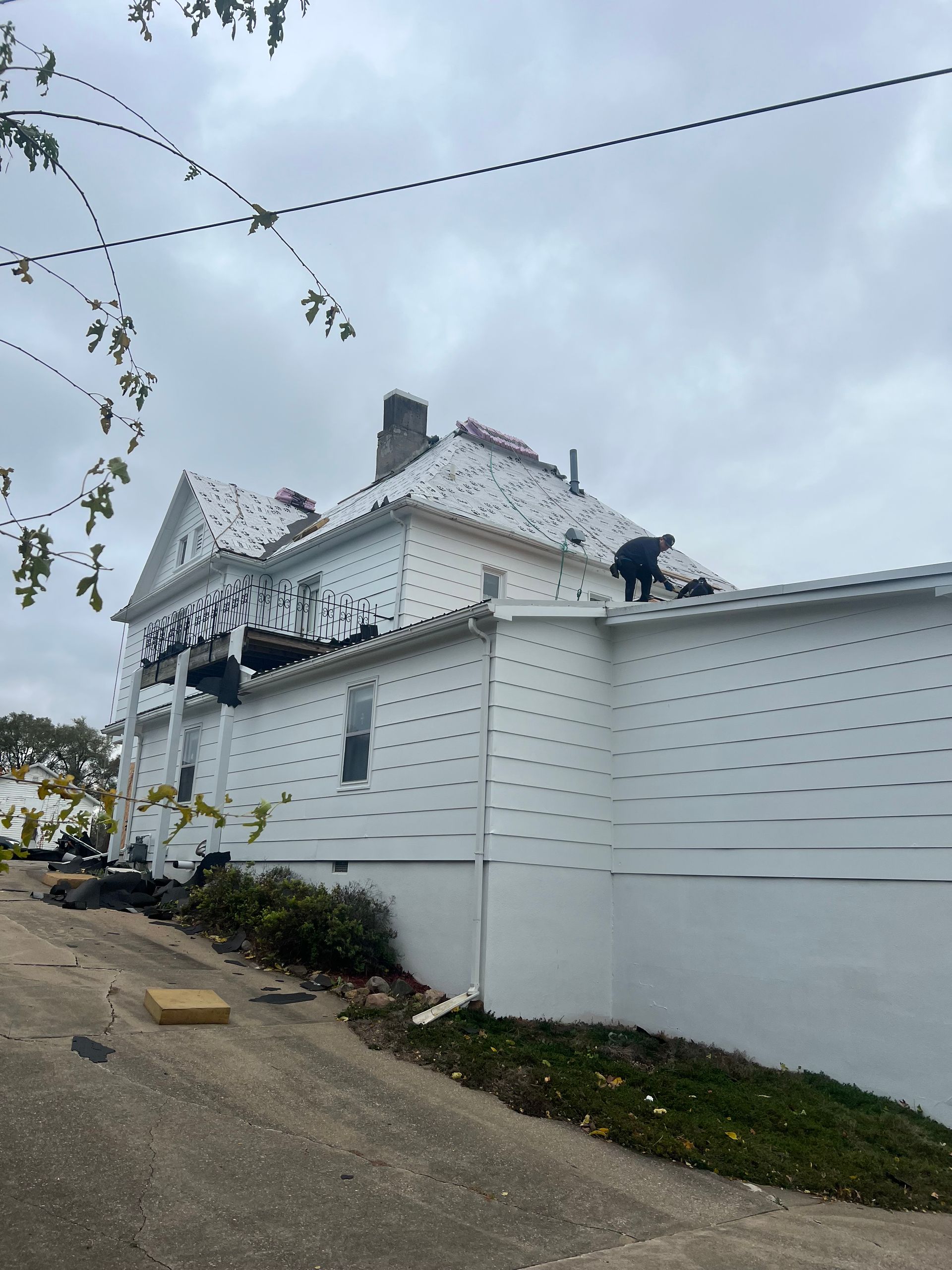 White house with roof damage. People on roof. Cloudy sky.
