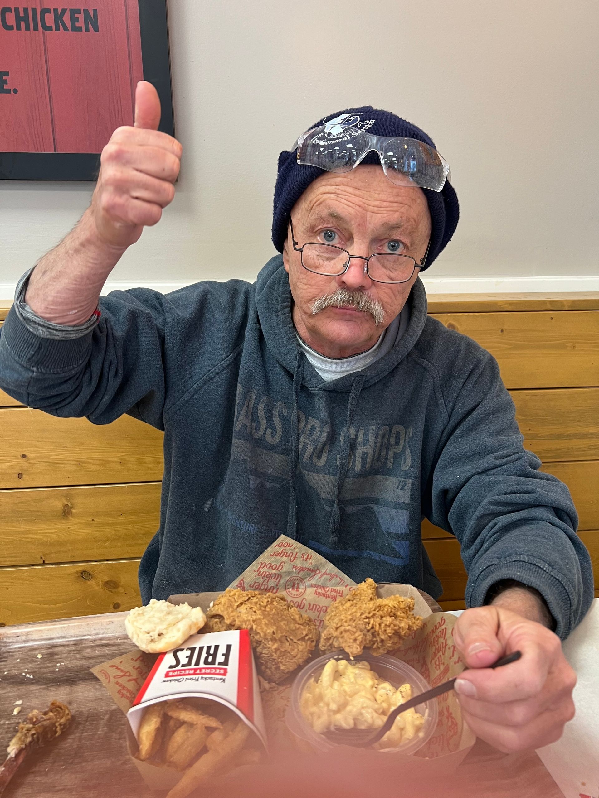 Man giving thumbs up, enjoying fried chicken, fries, and mac and cheese at a restaurant.