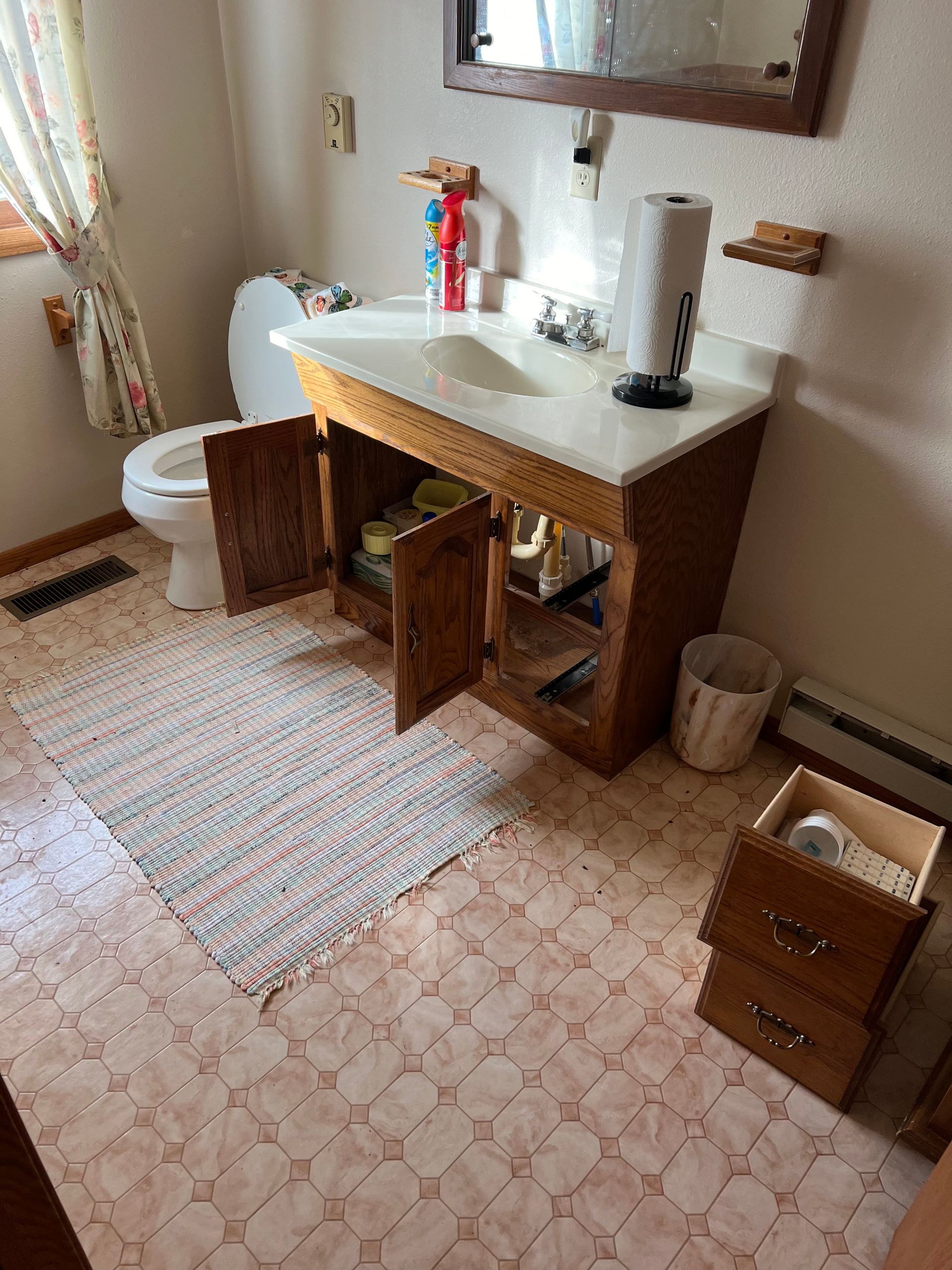 Bathroom with a sink, toilet, cabinet, rug, and open drawers.