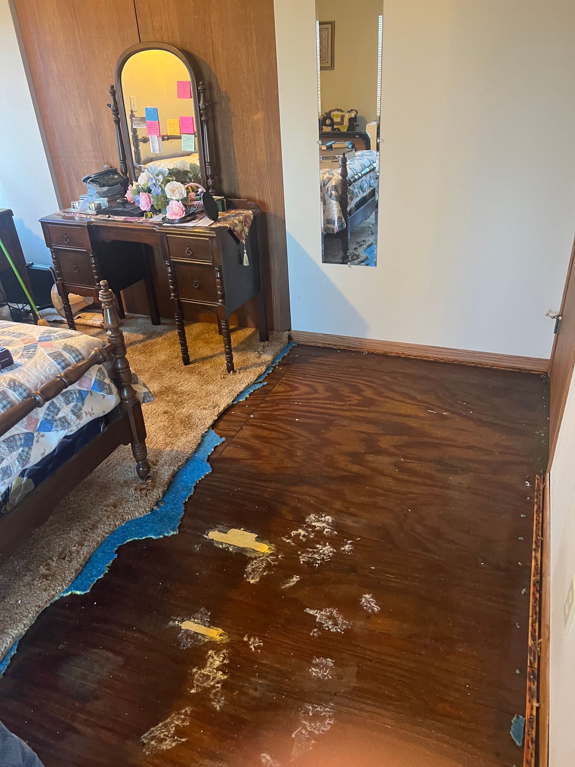 Bedroom with damaged wood floor, vanity, bed. Floor has blue, peeling paint.