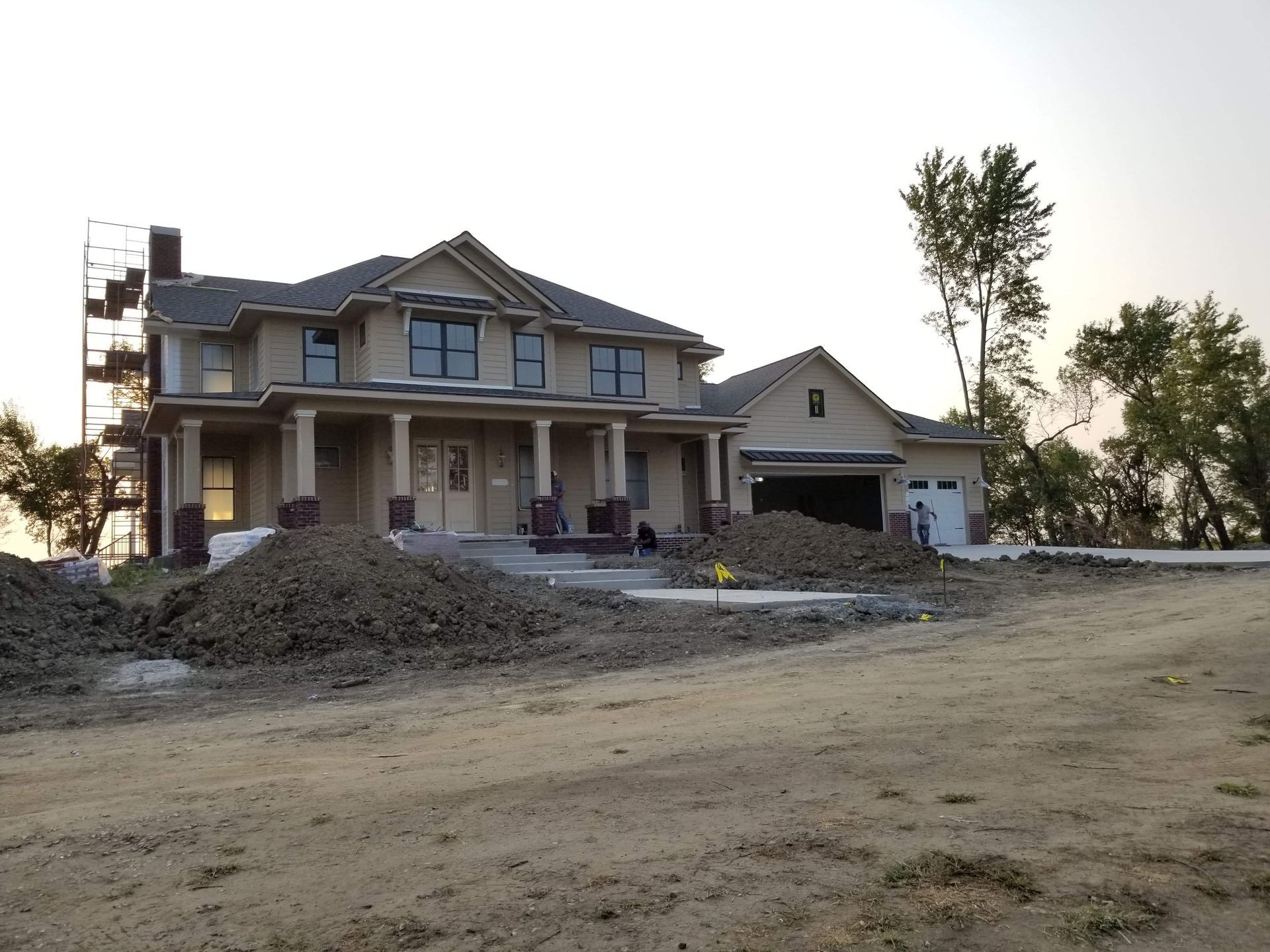 Newly constructed two-story house with attached garage, surrounded by dirt and construction materials; set against a dusky sky.