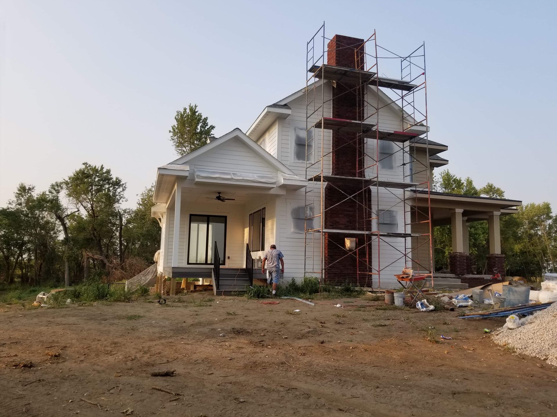 White house under construction; brick chimney, scaffolding, person near front door.