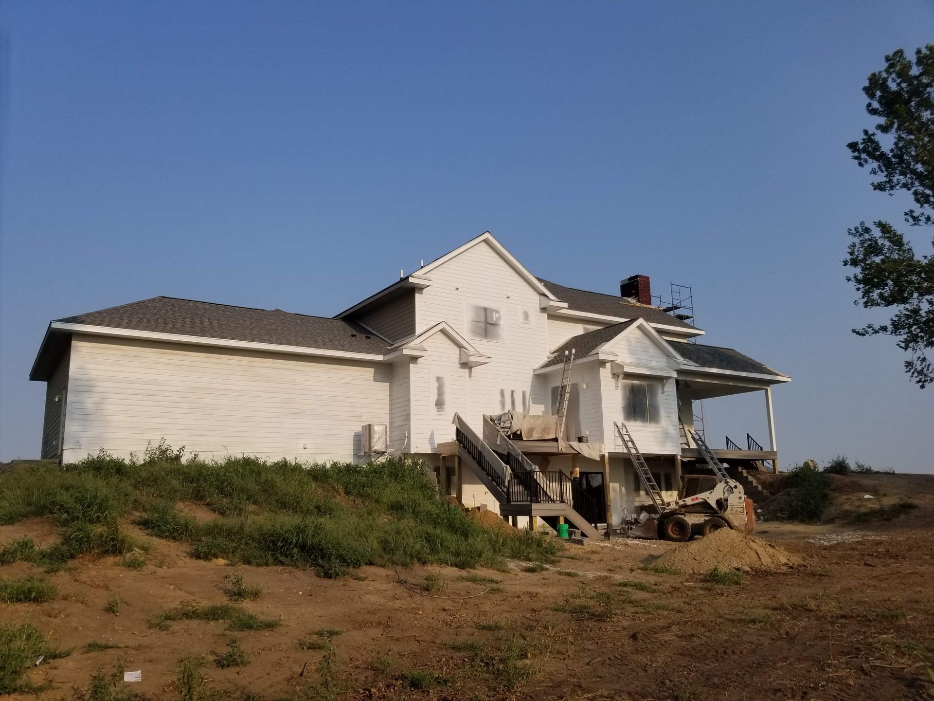 A two-story white house under construction with a dark roof and a small porch.
