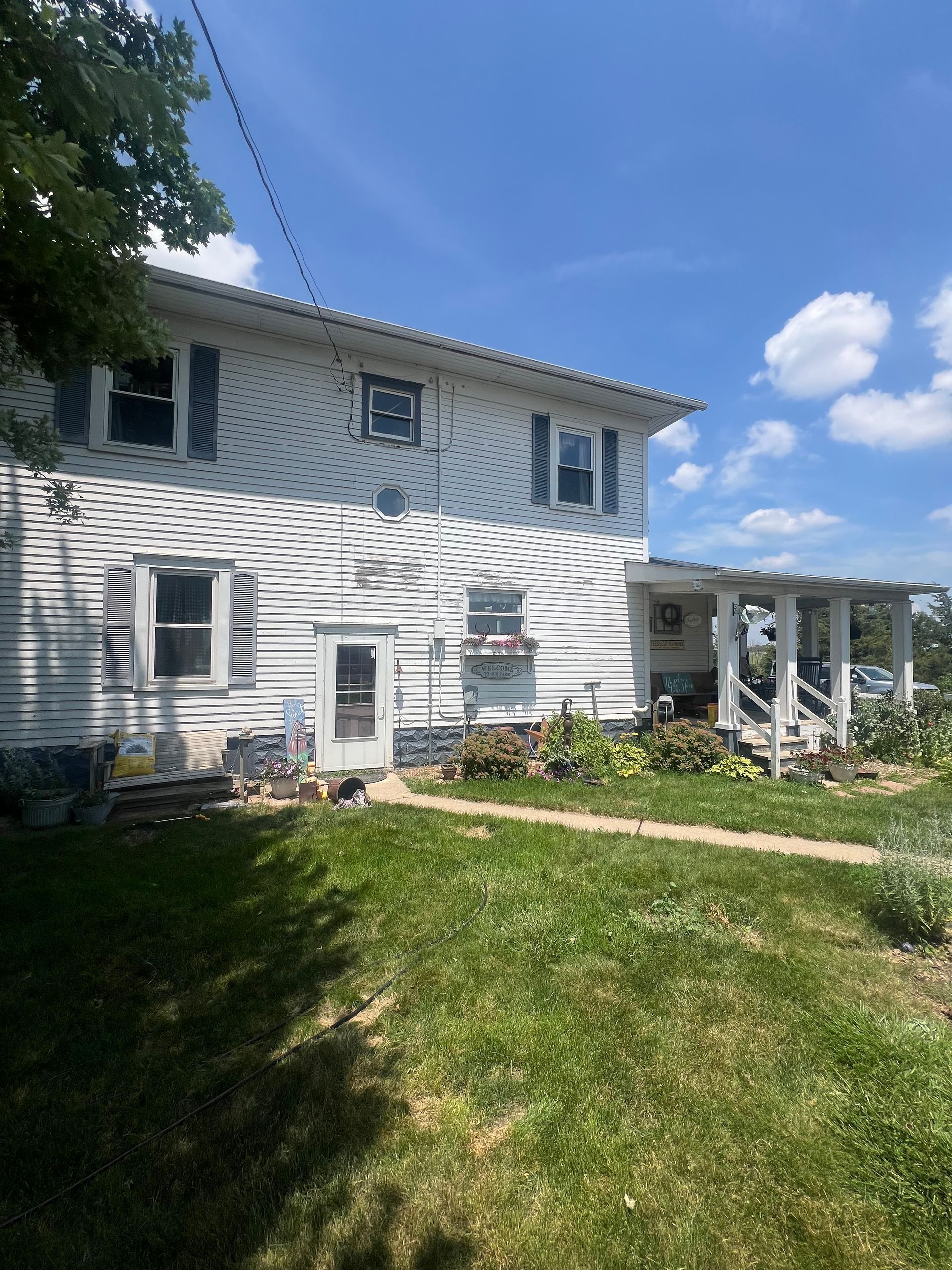 Two-story white house with a porch. Green lawn and blue sky.