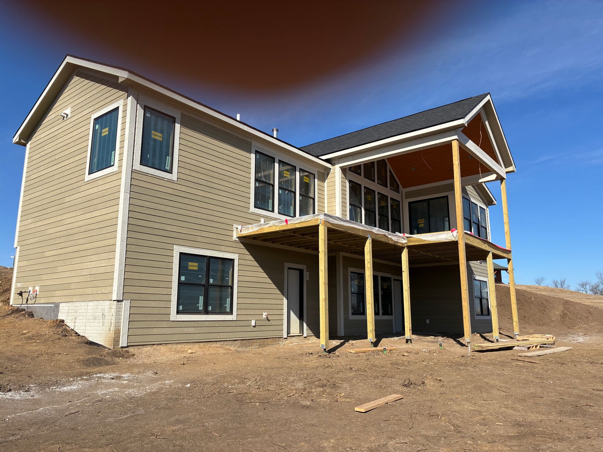New house under construction with light brown siding, black windows, and wooden deck.