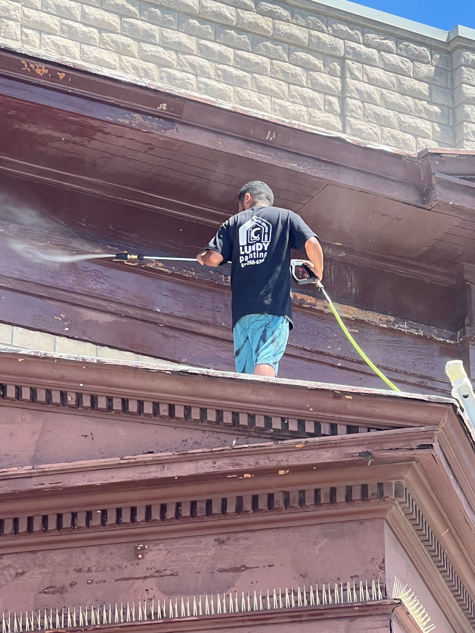 Person power washing the exterior of a brown building.