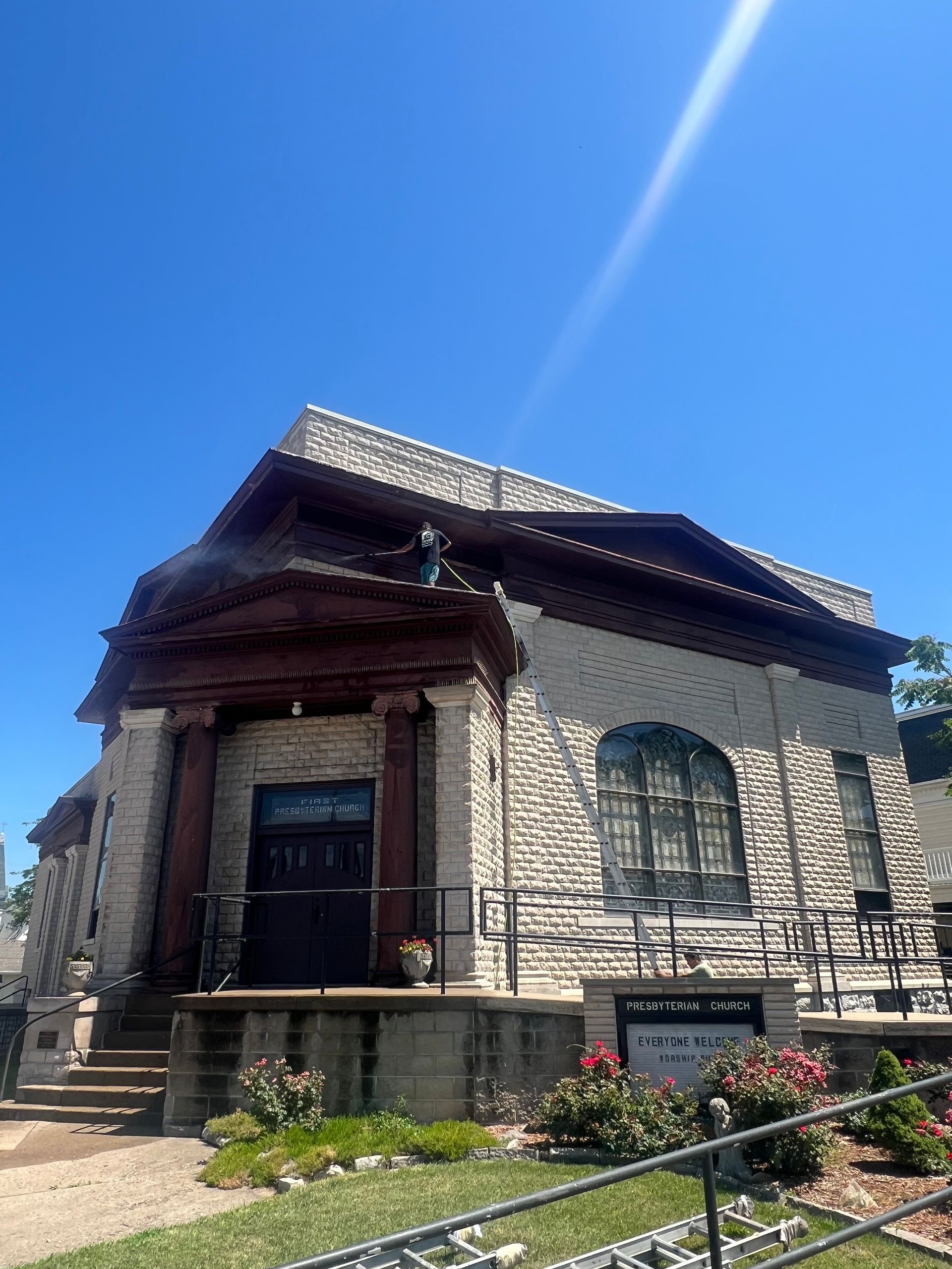 Stone church with dark doors, red trim, and rose bushes against a bright blue sky.