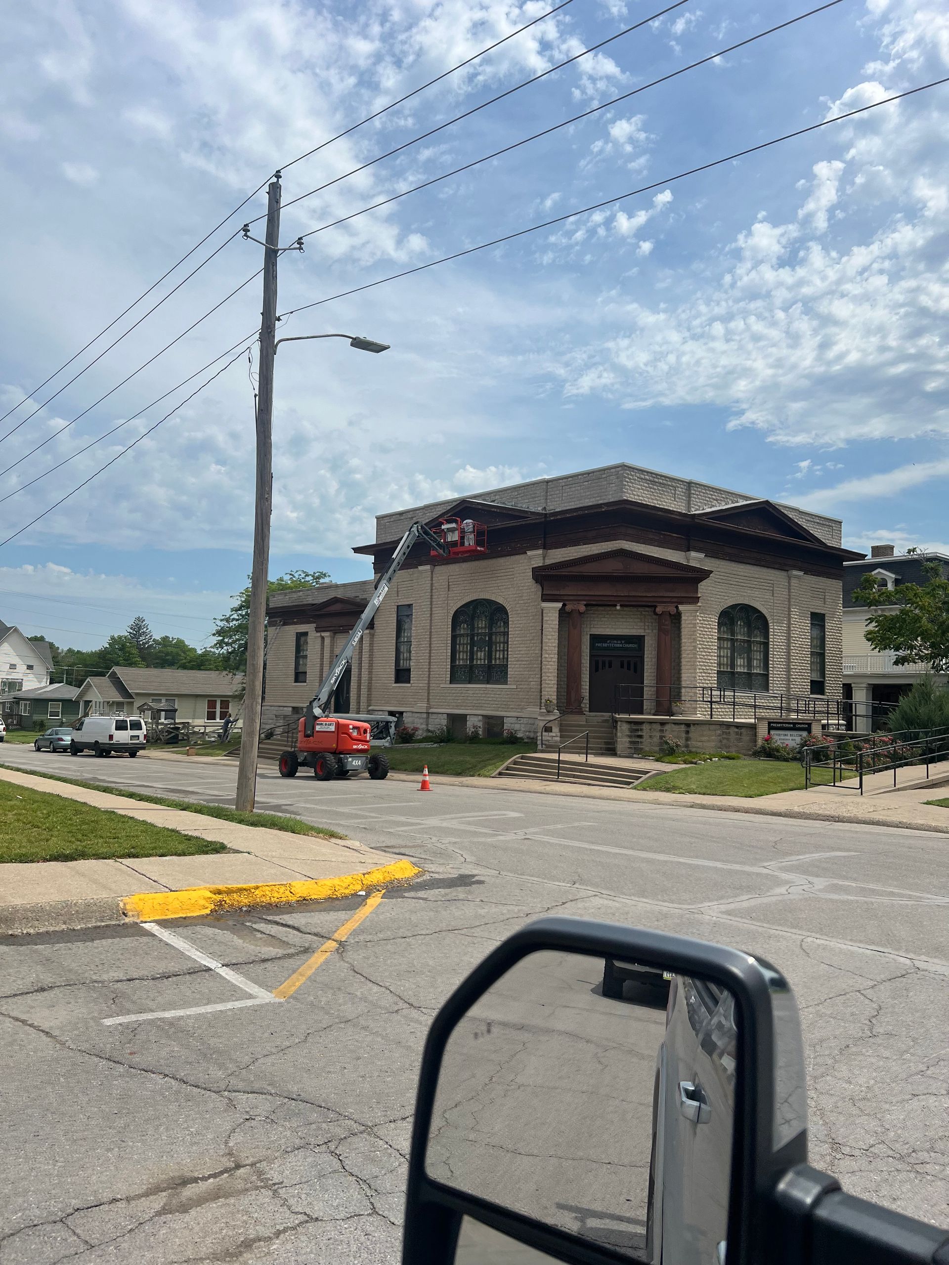 Exterior of building with lift, utility pole, and parked vehicles. Clear sky.