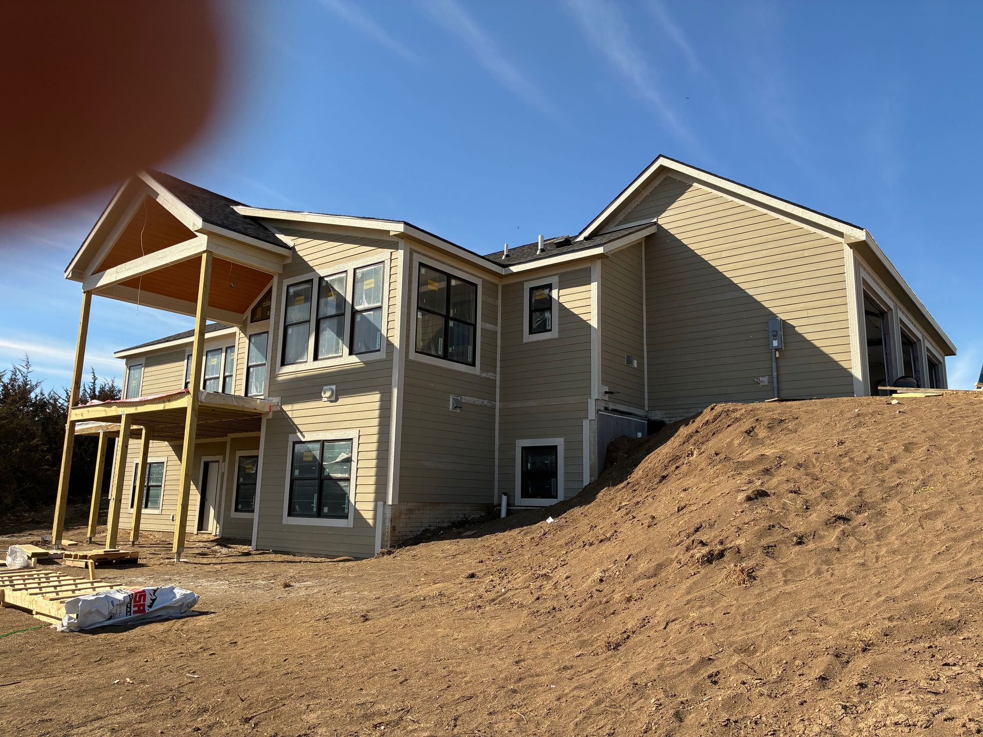 Tan house under construction on a hillside with an open porch and blue sky.