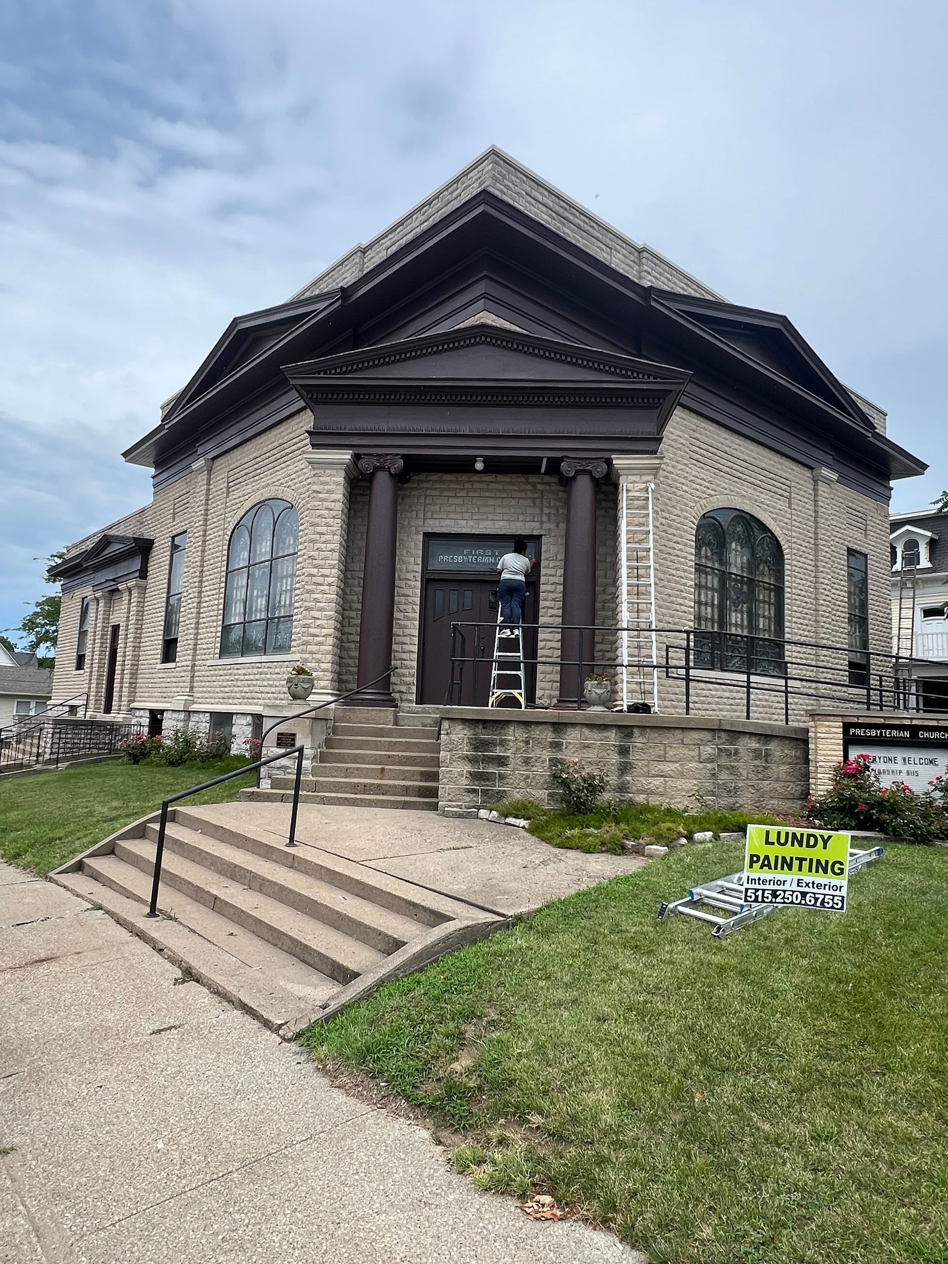 Stone church with columns, steps, and a person working at the entrance. 