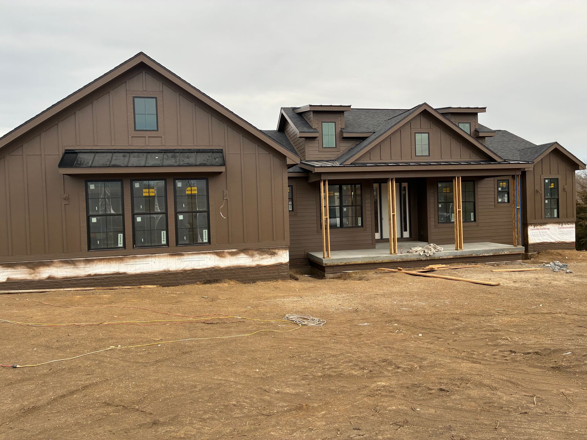 Brown house under construction with multiple windows and a porch on a cloudy day.