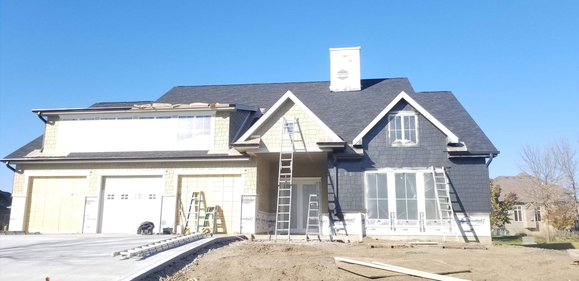 House under construction with garage, front door, and chimney against a blue sky.