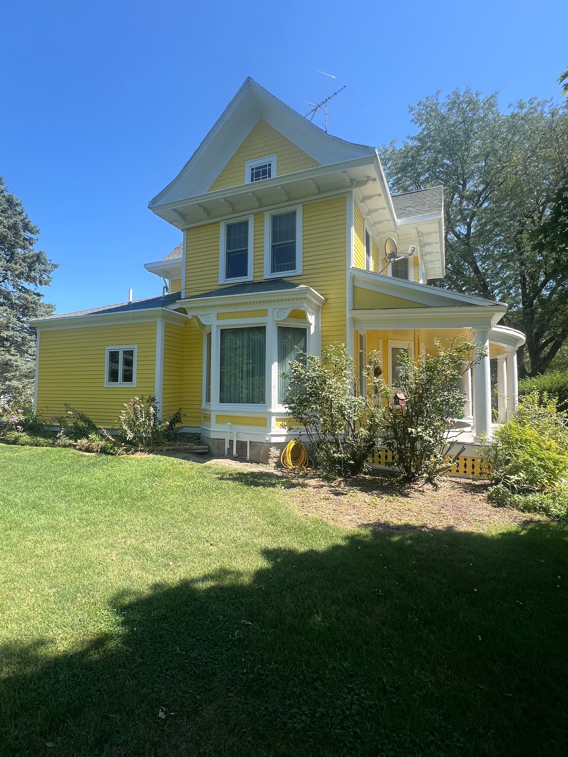 Yellow Victorian house with white trim, green lawn, and sunny blue sky.
