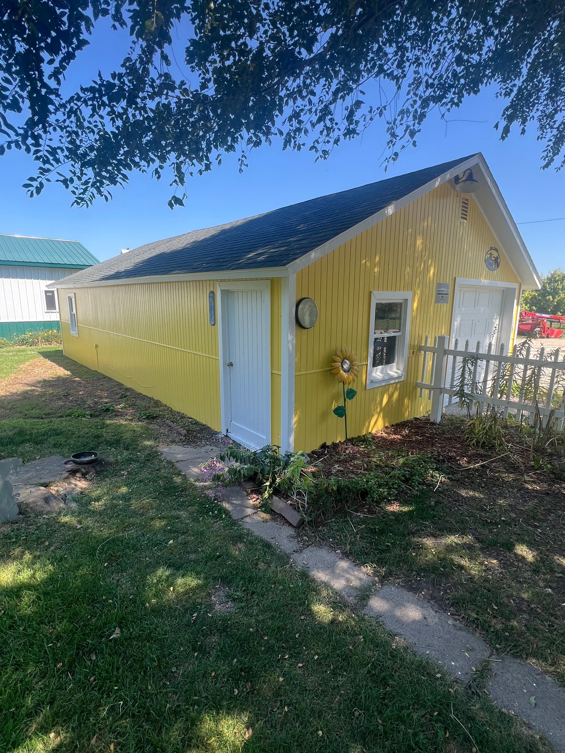 Yellow building with white doors and window, small picket fence, on a sunny day.