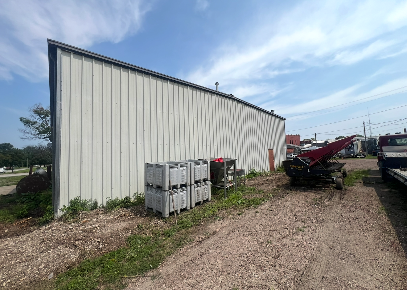 Warehouse with gray siding, parked equipment, gravel ground, and blue sky.
