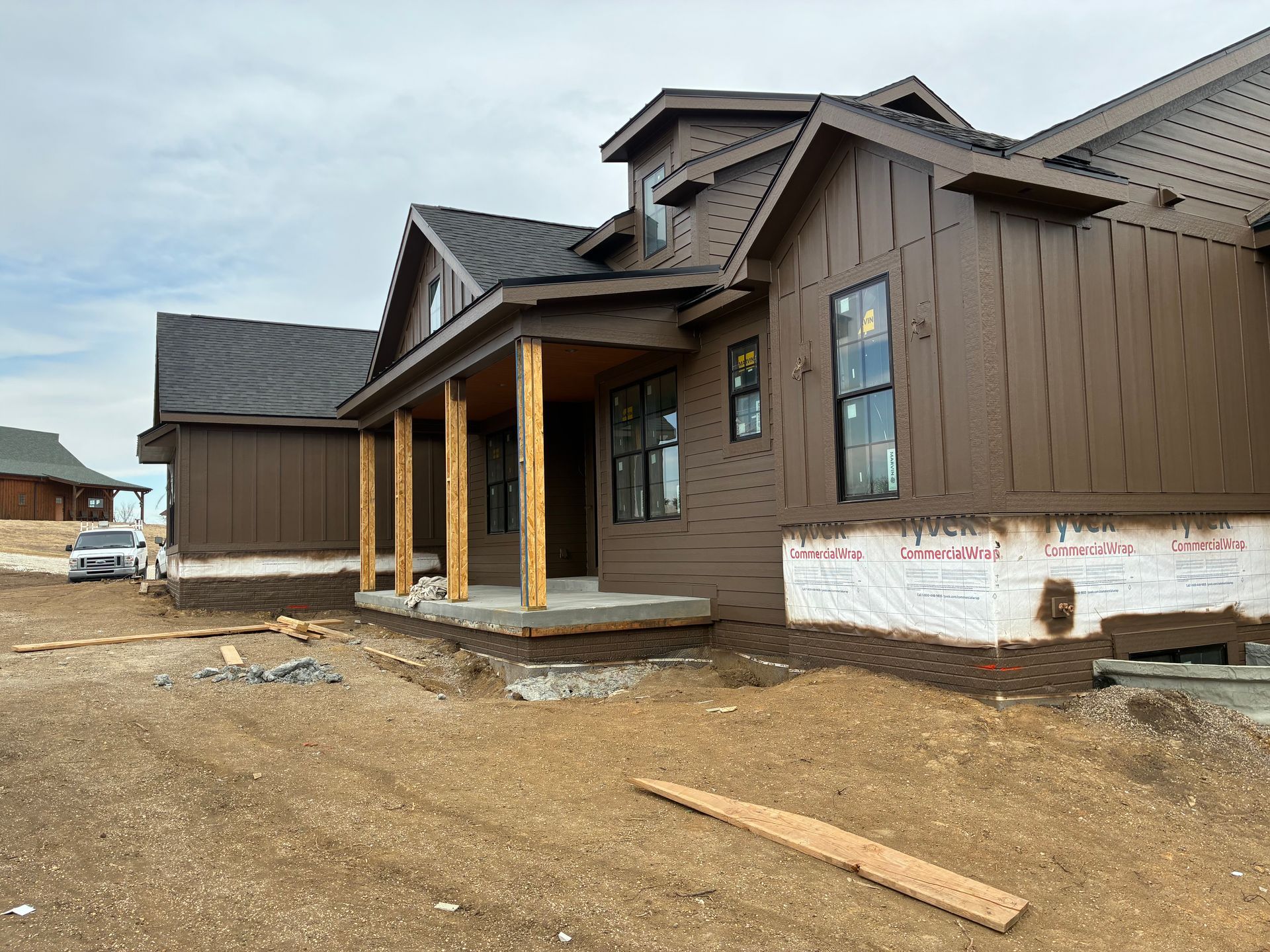 Brown house under construction with porch and dark roof against a cloudy sky.
