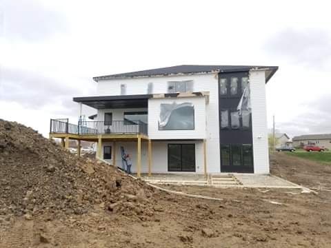 New two-story house under construction with white siding, black trim, large windows, and a deck.