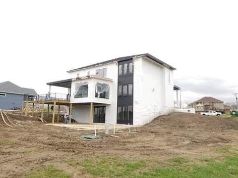 Two-story white house with a partially built deck. Dark trim and windows. Construction site with dirt and grass.