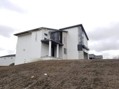 Two-story house under construction on a small hill, exterior covered in white siding and dark accents.