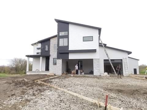 Modern two-story house under construction with black, white, and gray exterior. Workers and concrete forms are visible.