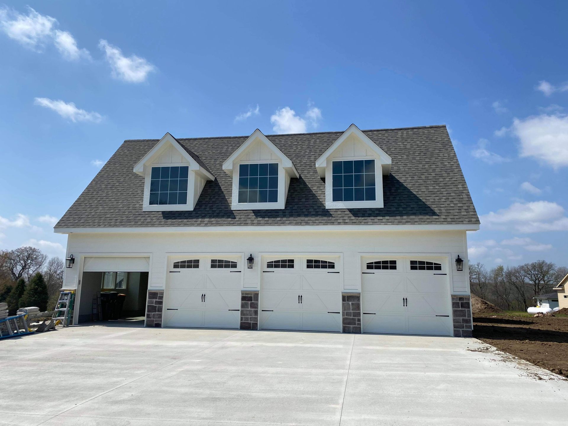 Three-car garage with dormers and white doors under a blue sky.