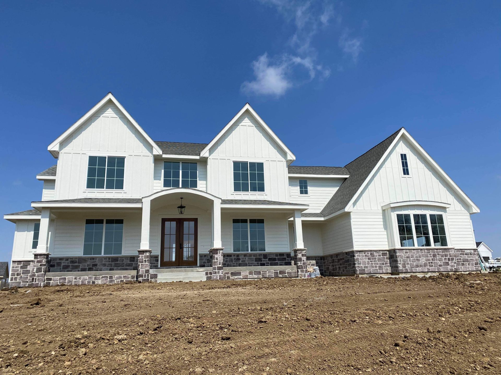 White two-story house with a gray roof and stone accents, under a clear blue sky.