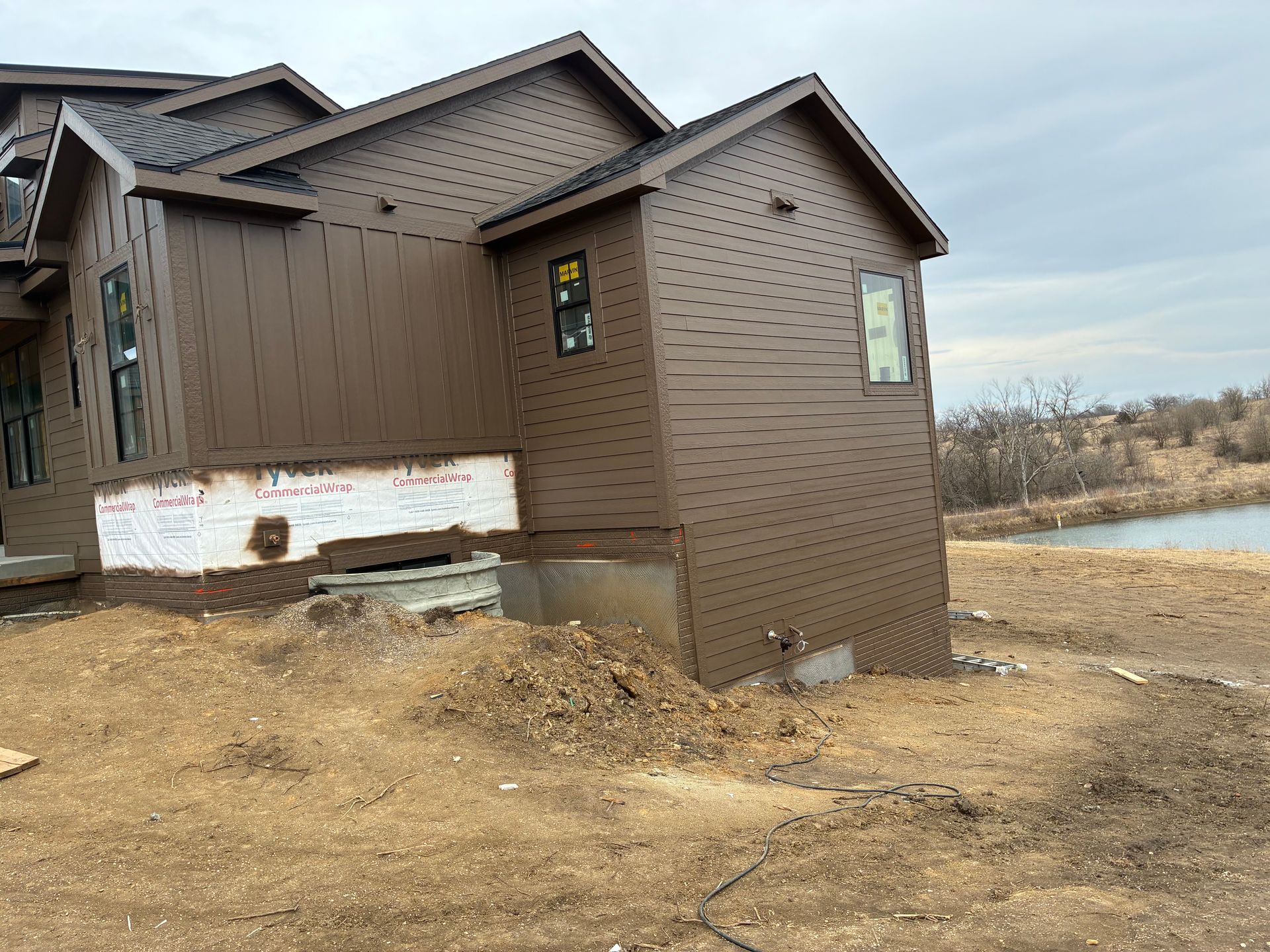 Brown house under construction near a body of water; dirt and debris visible.