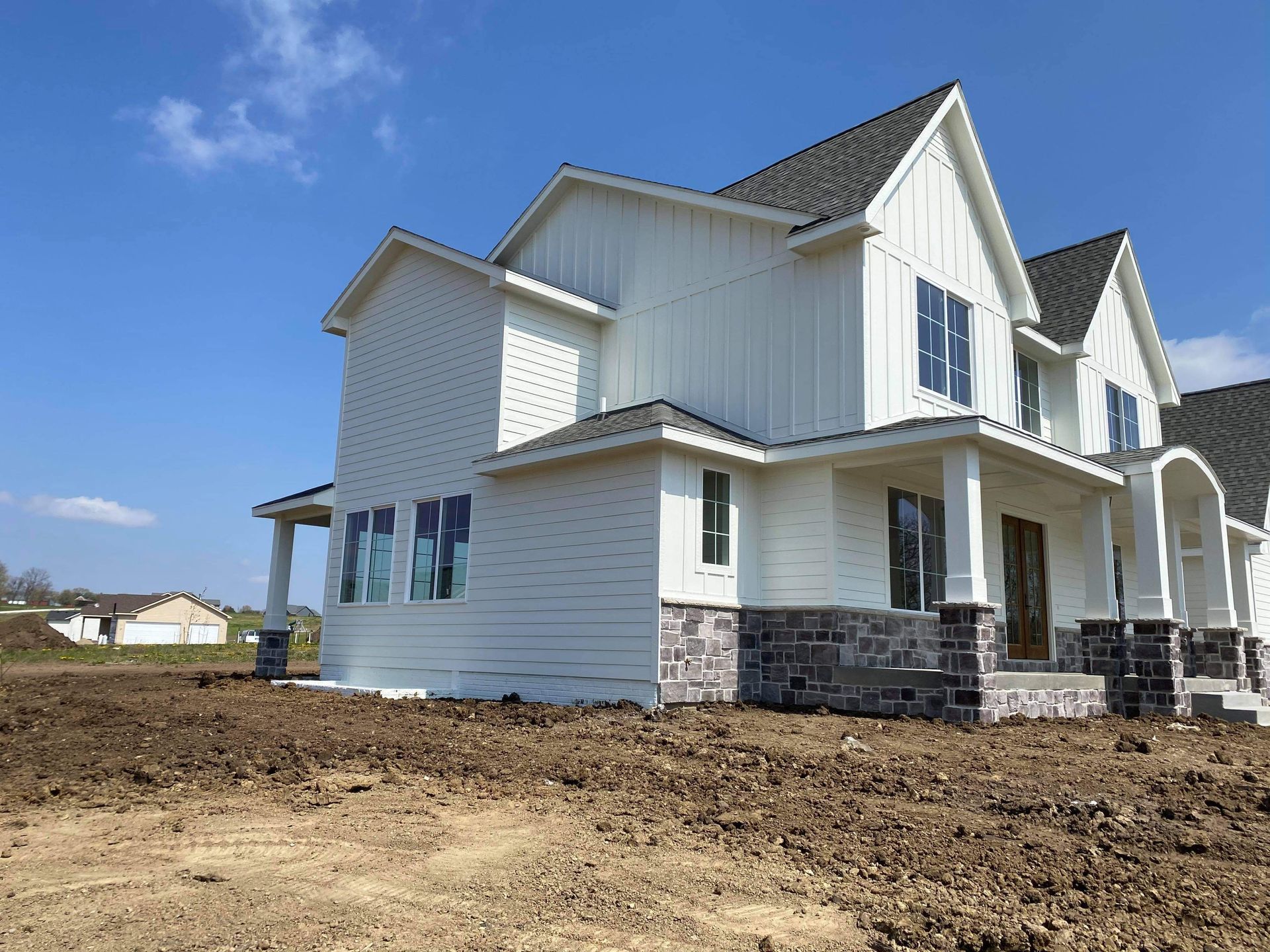 New white house under construction, with gray stone base, against a blue sky.