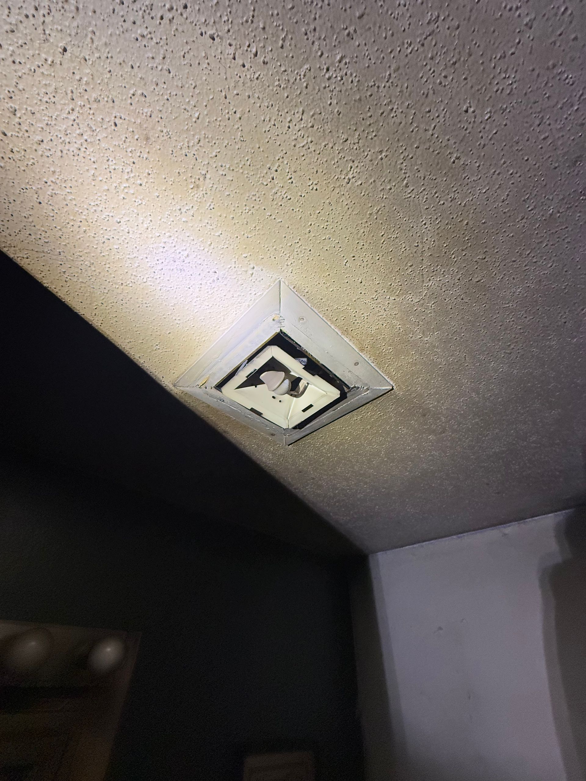Ceiling air vent, surrounded by popcorn texture, with dark discoloration.