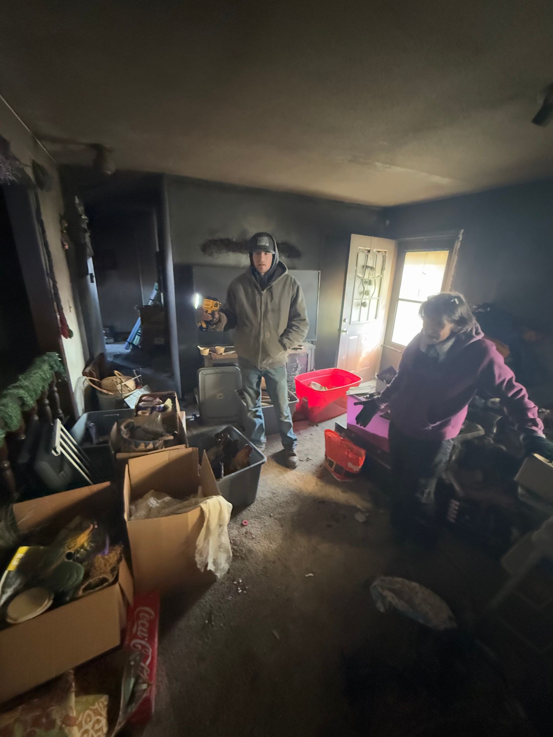 Two people stand in a room damaged by fire, surrounded by debris and soot.