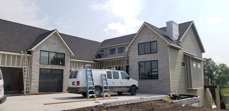 House under construction with brick and siding, a van parked in the driveway, and framing exposed.