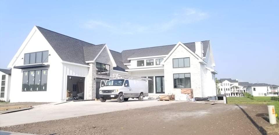 White house with dark roof and large windows under construction; van parked in the driveway.