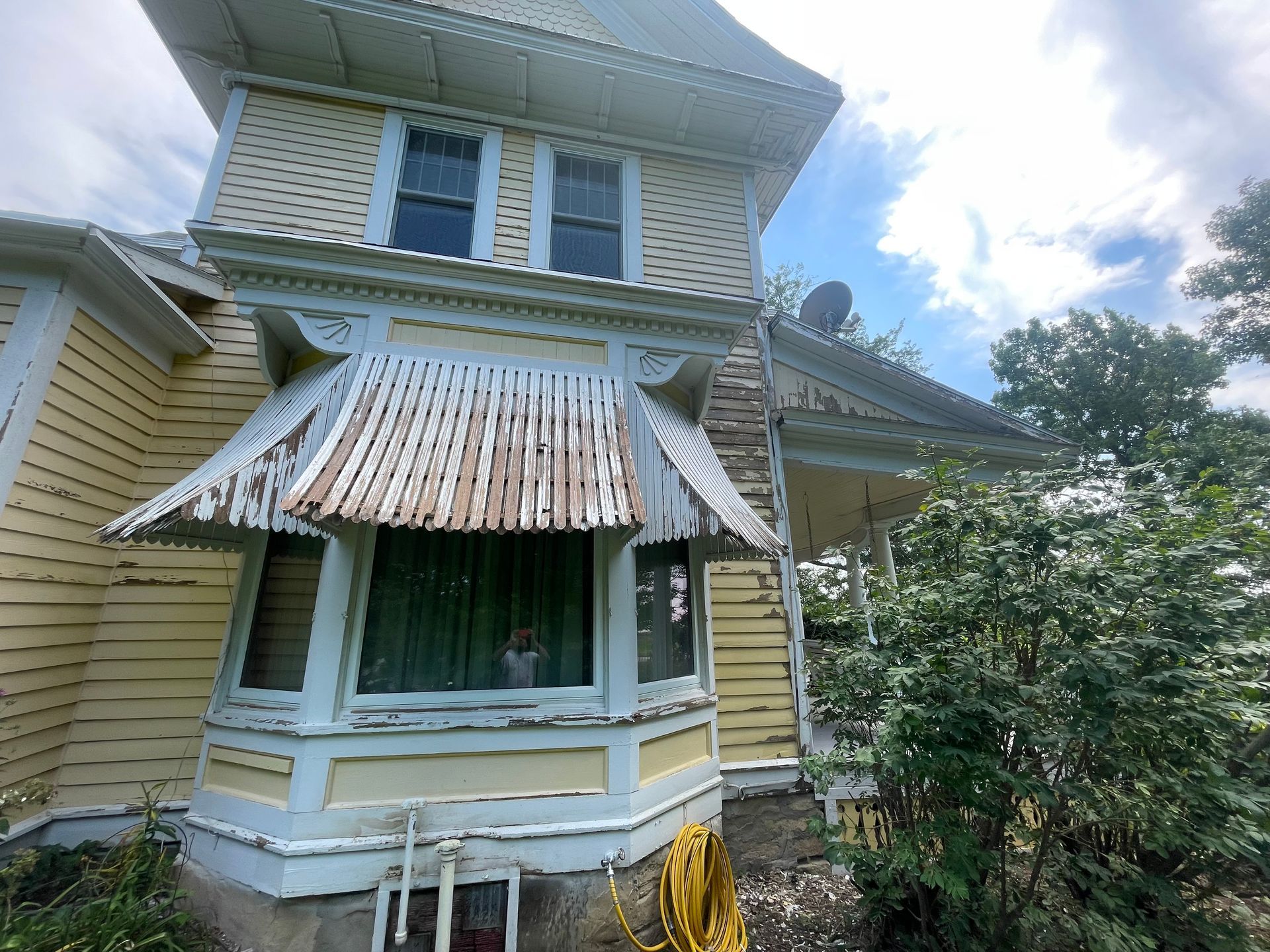 Yellow Victorian house with peeling paint and bay window.