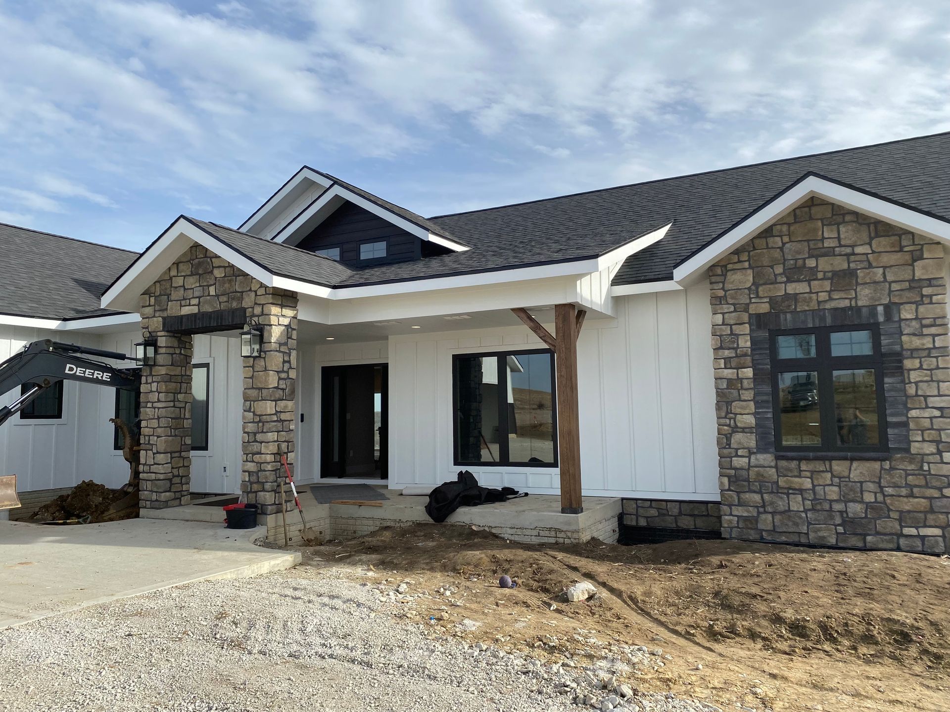 New construction house with stone and white siding, dark roof, and blue sky.
