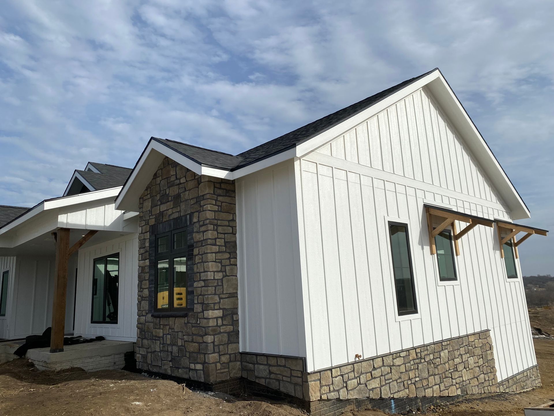 New house under construction, with stone and white siding. Black roof. Cloudy sky.