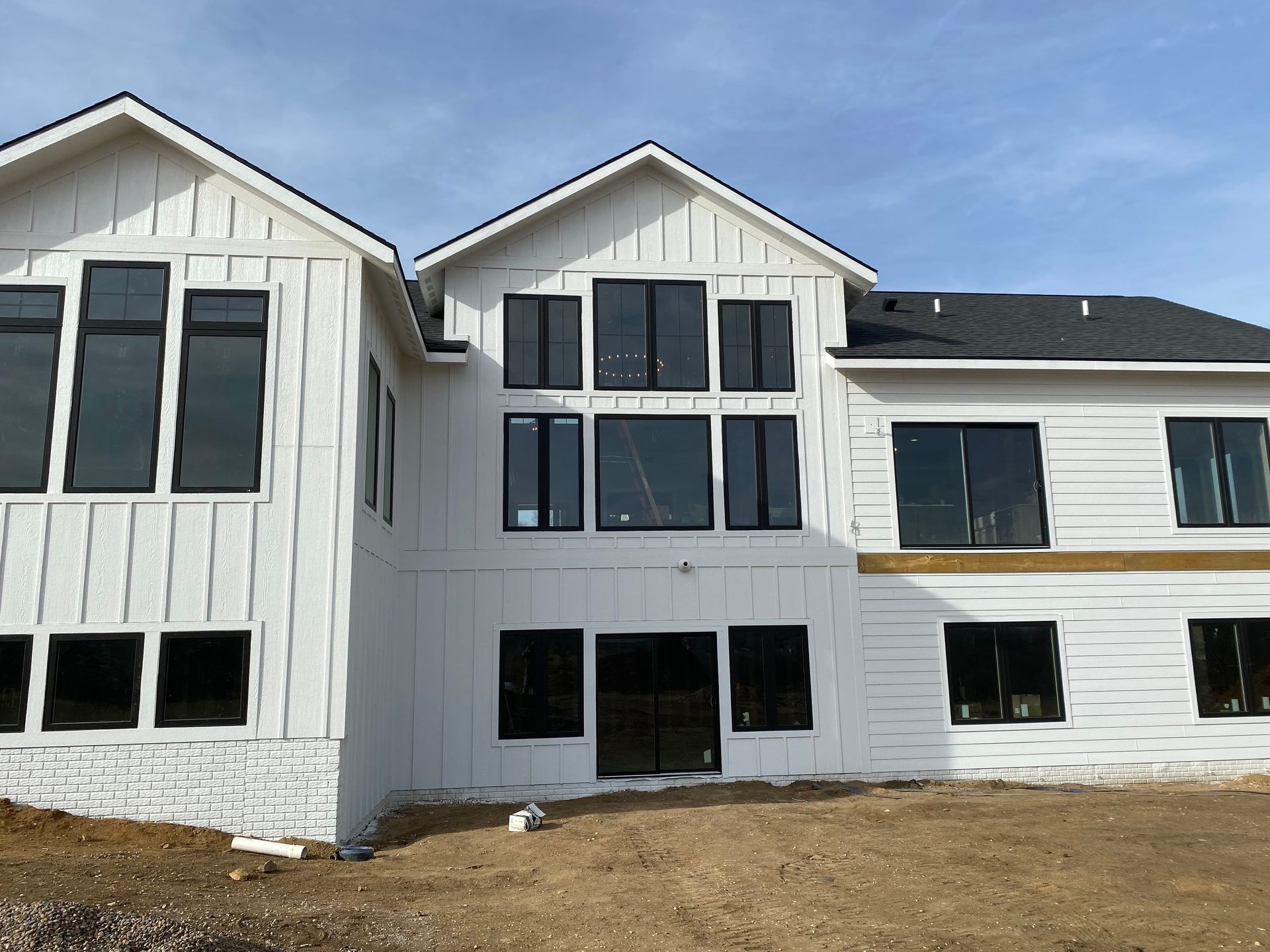 White house exterior with black-framed windows, against a blue sky, under construction.