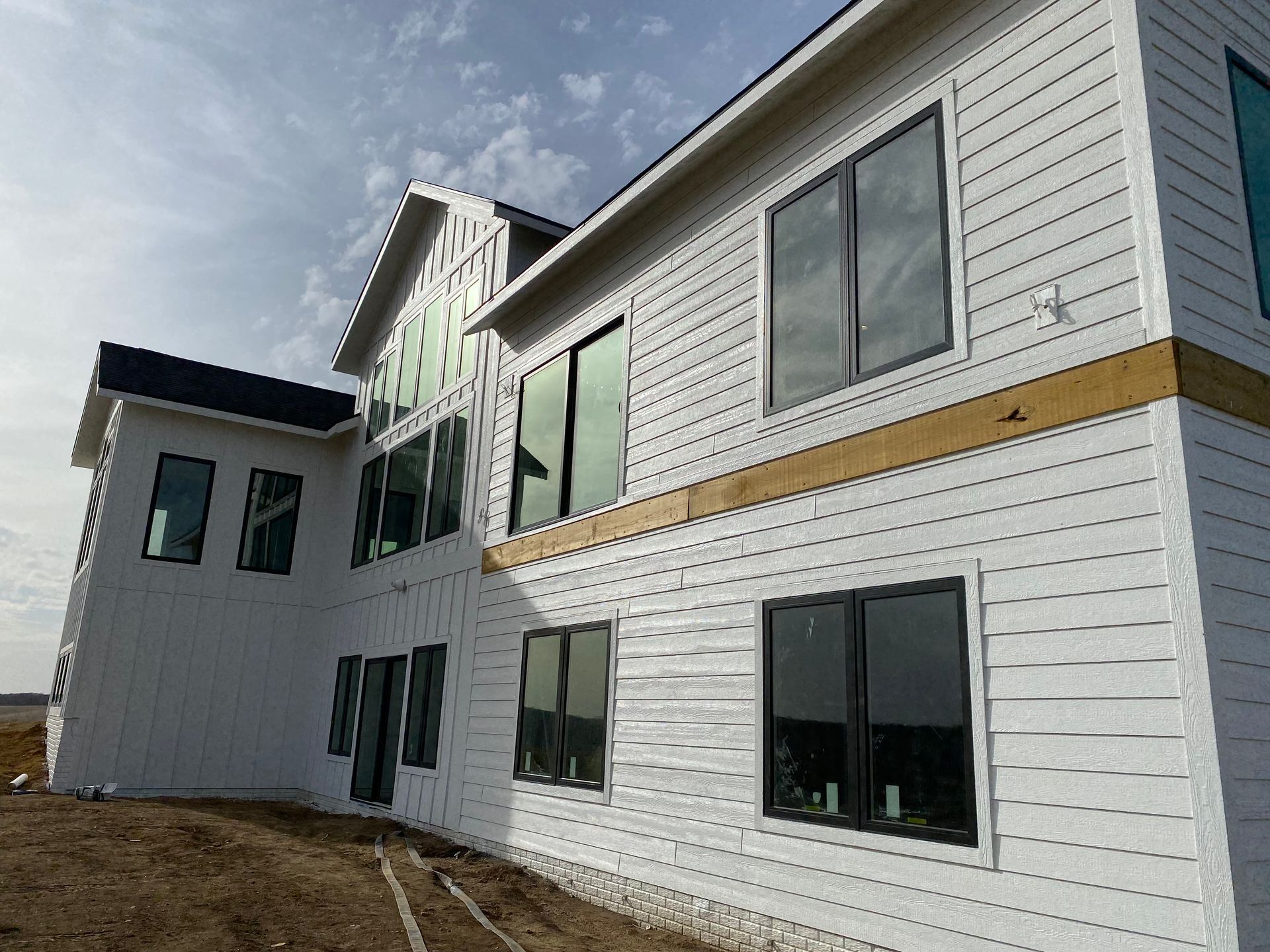 New, white house exterior with black-framed windows, under construction, blue sky.