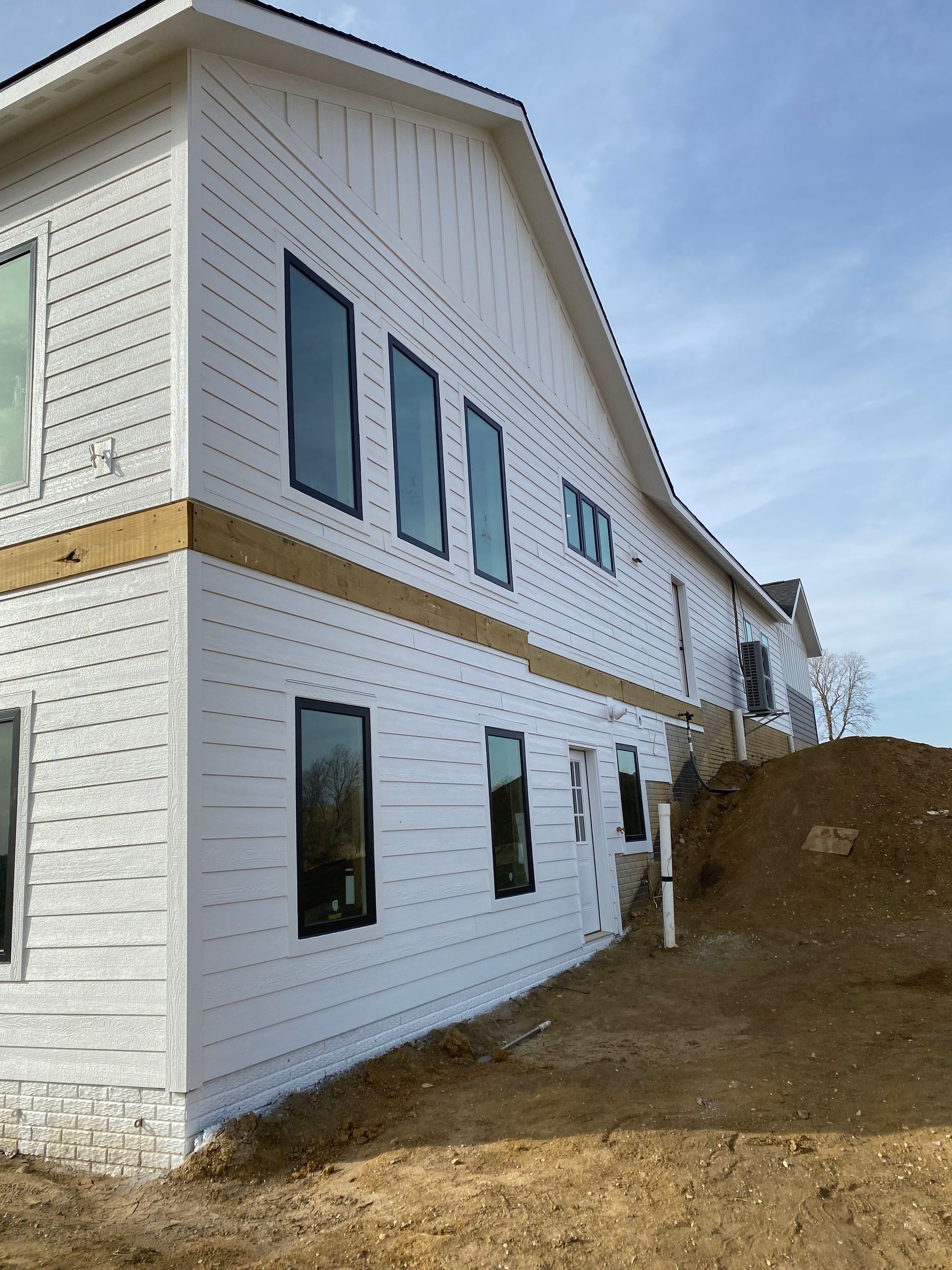 Building under construction; white siding, black windows, beige trim, on a slight hill against a blue sky.