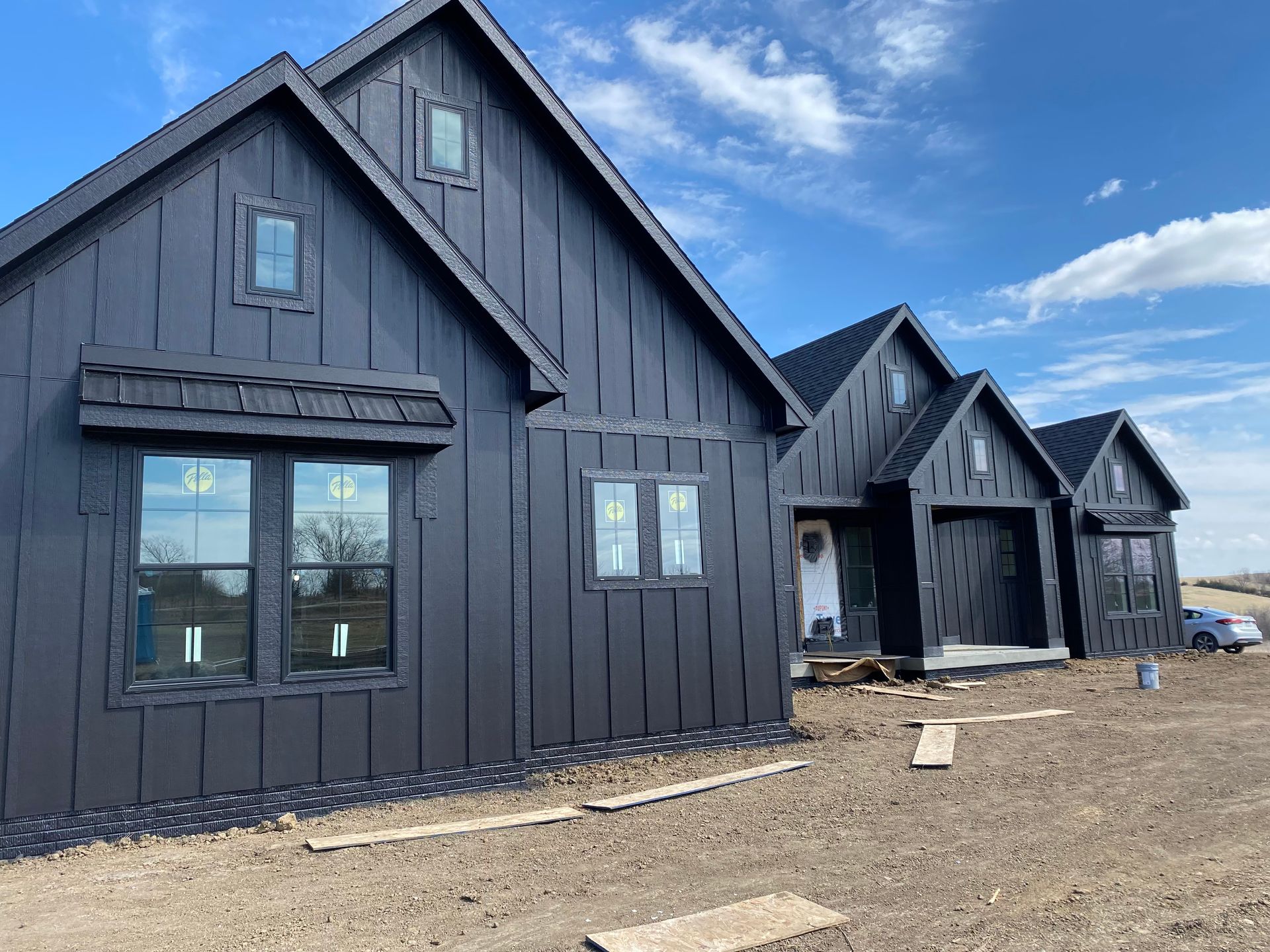 Black-sided modern homes under construction against a partly cloudy sky.